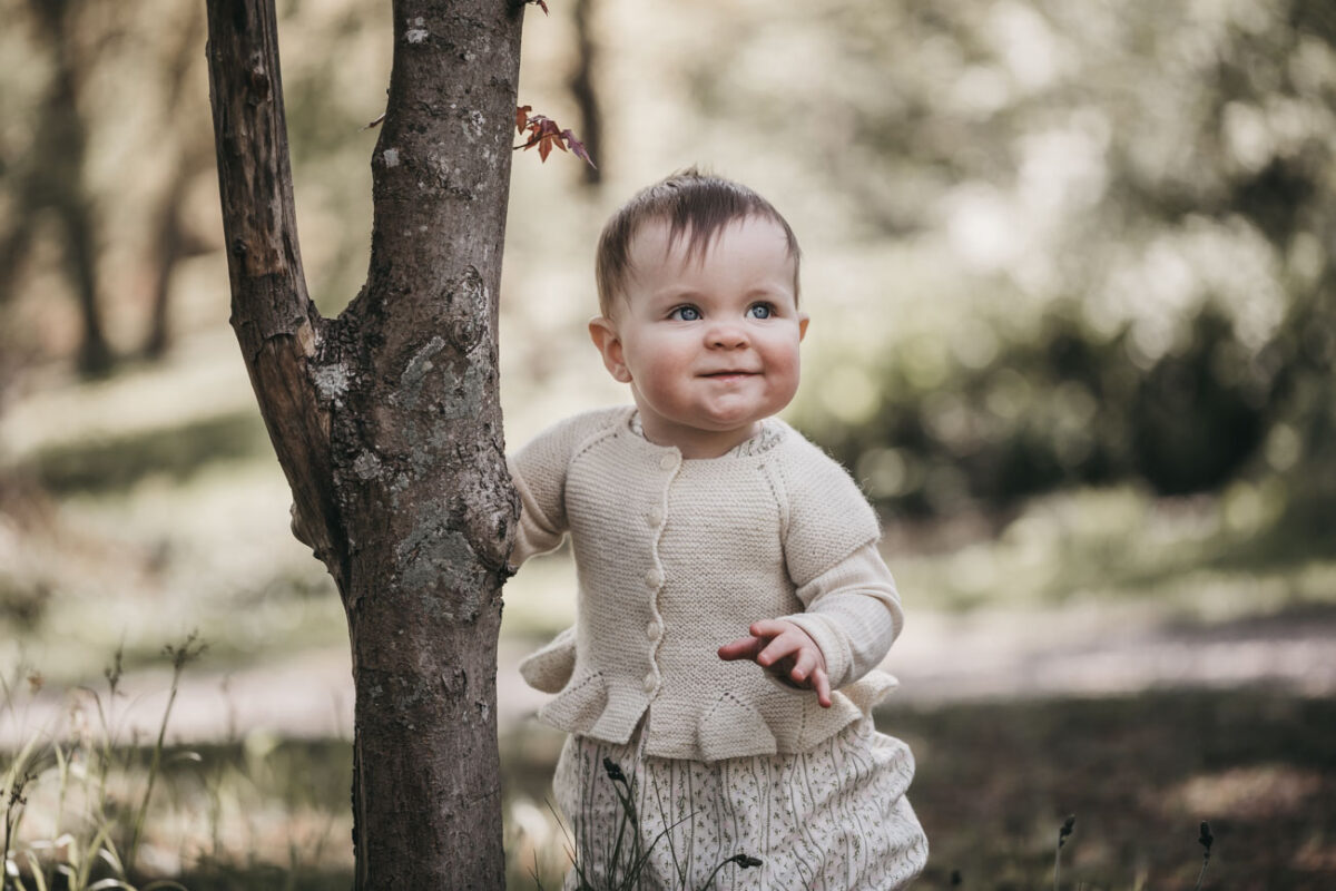 baby står ved træ under babyfotografering